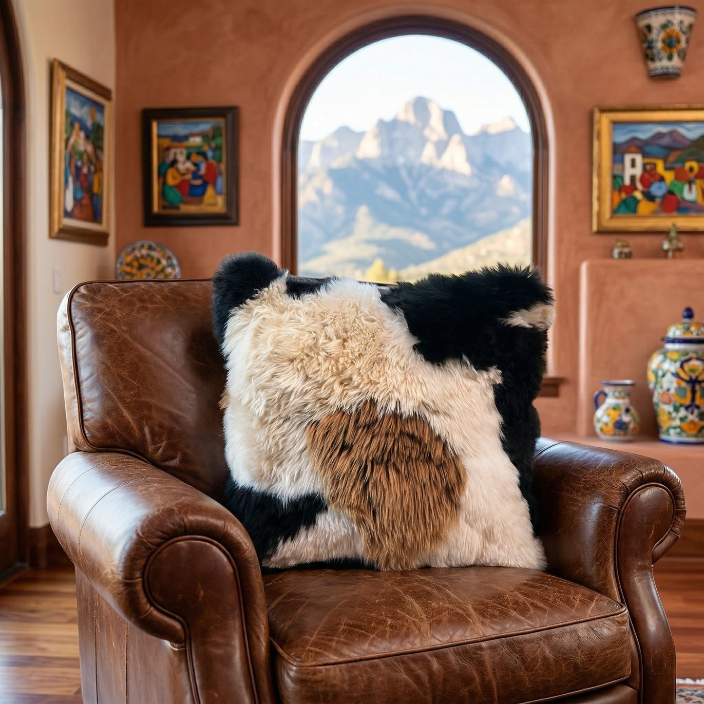 Peruvian Accent mosaic baby alpaca fur pillow with black, white, and brown patches on a leather armchair.