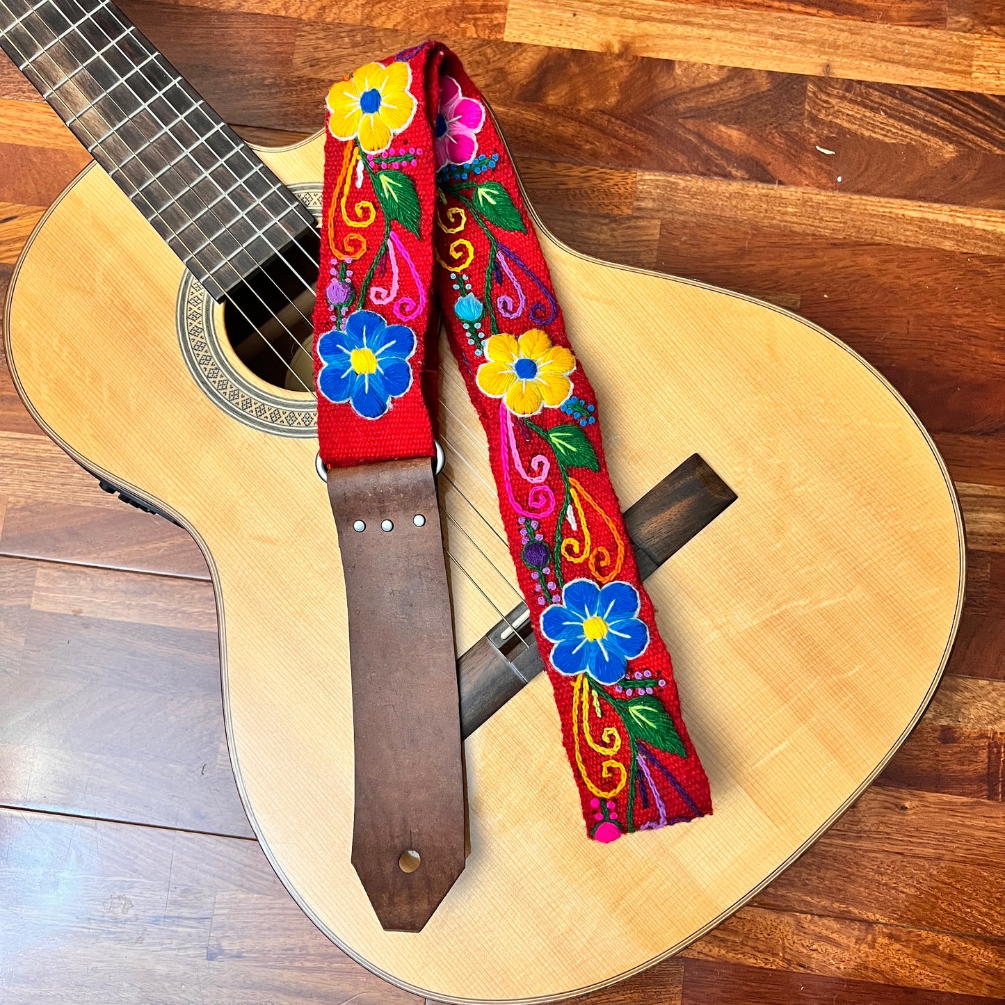 Red Floral handmade guitar Strap with hand cut leather ends. Laying over a guitar.