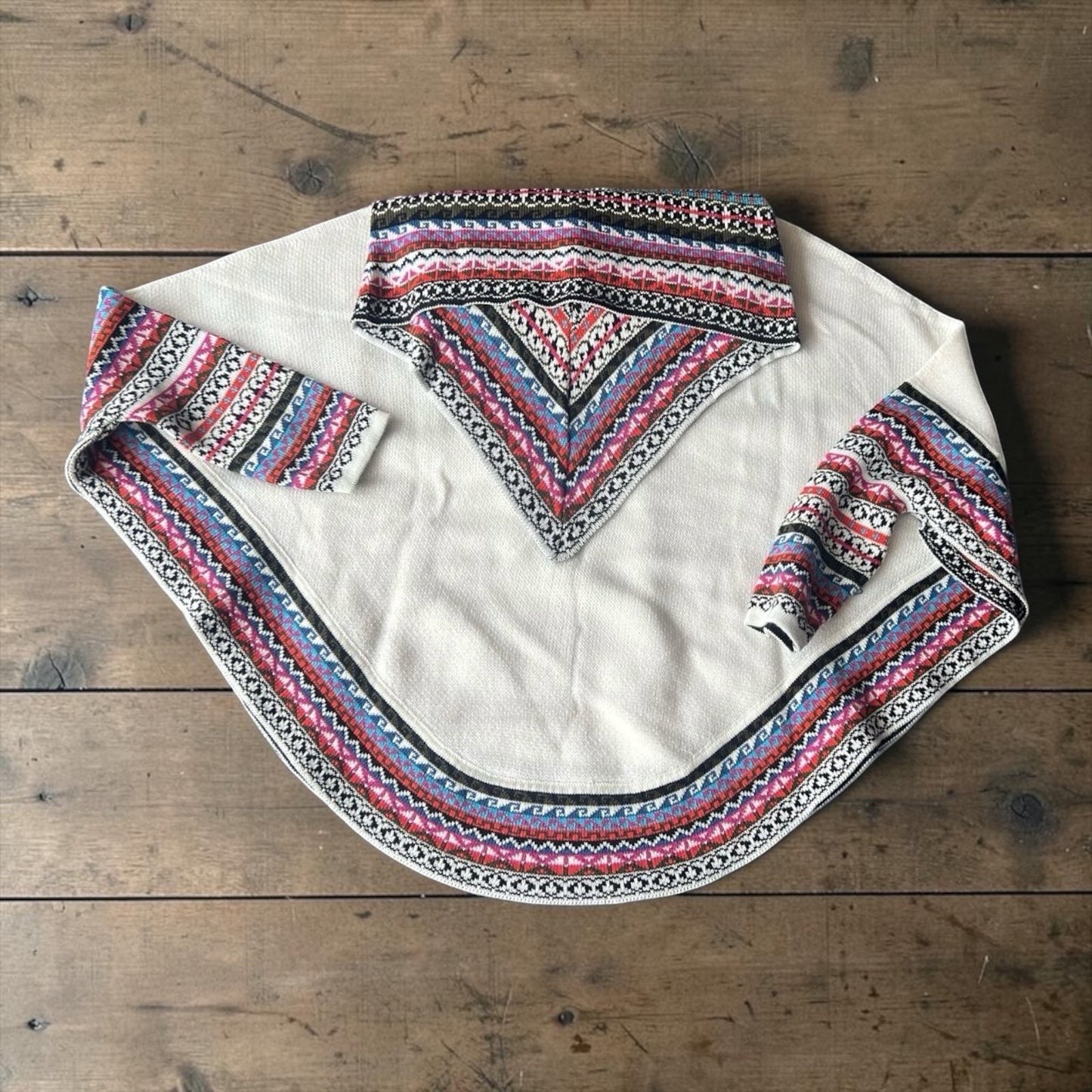 Peruvian Accent cream alpaca poncho with sleeves, featuring a colorful geometric pattern on the collar, cuffs, and hem.