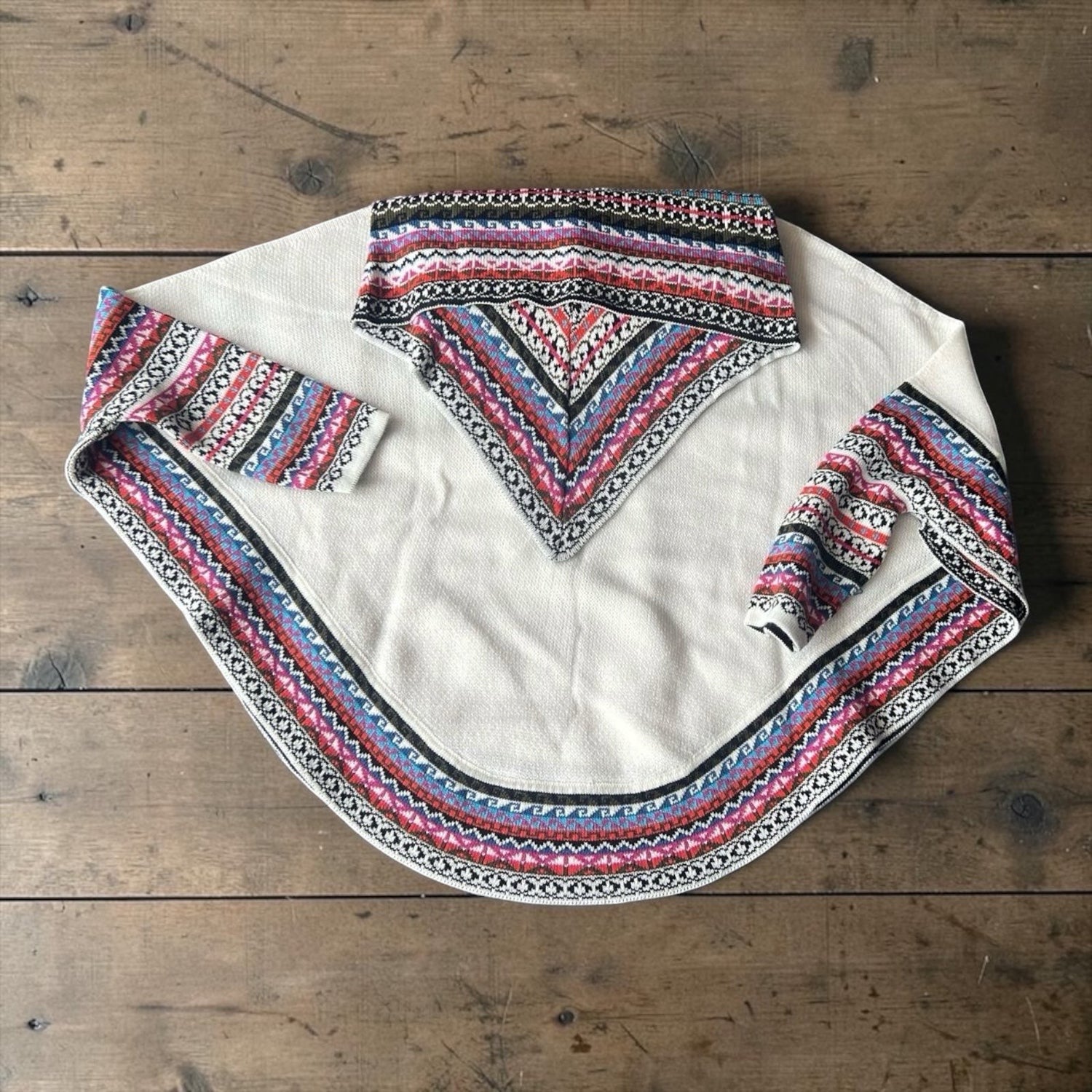 Peruvian Accent cream alpaca poncho with sleeves, featuring a colorful geometric pattern on the collar, cuffs, and hem.