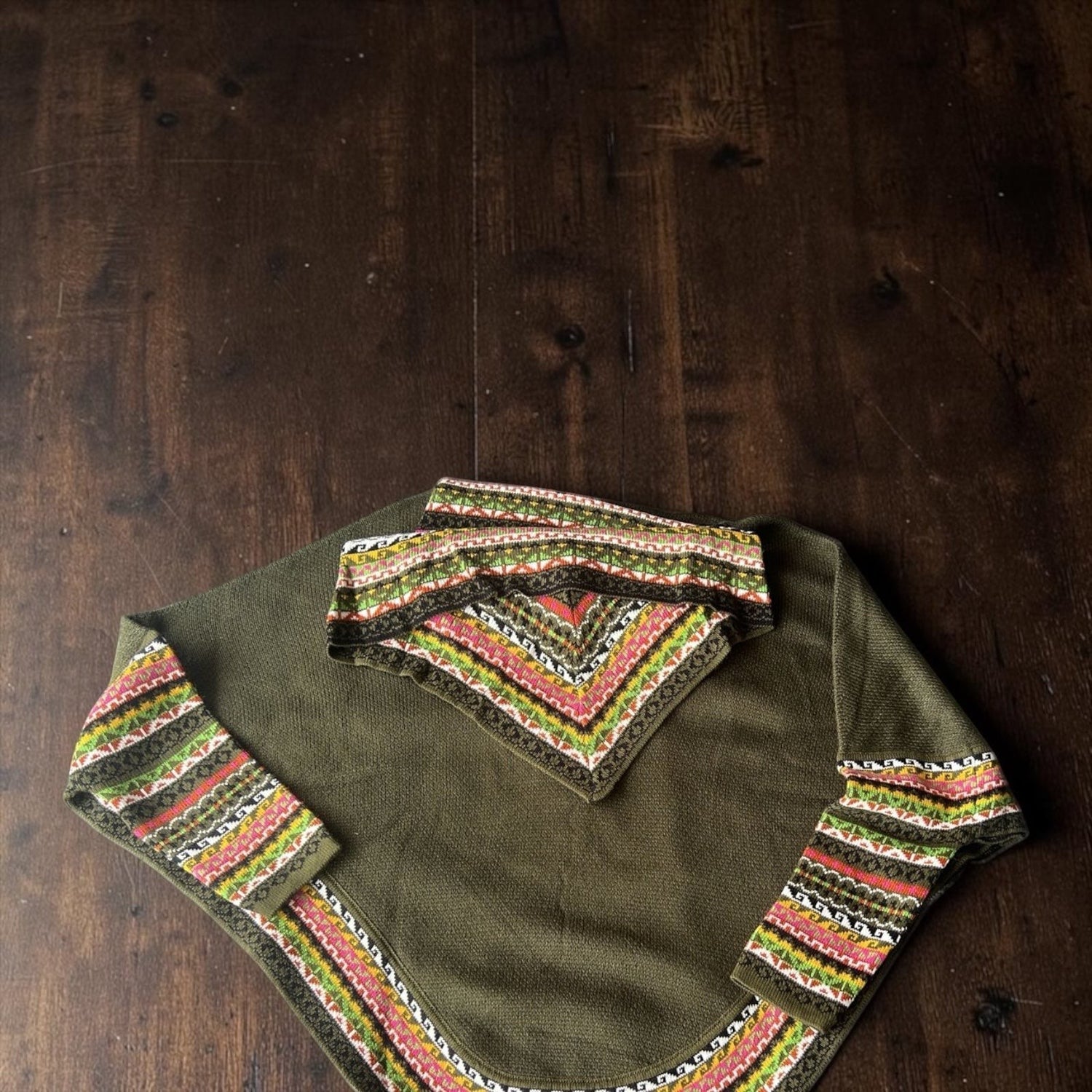 Peruvian Accent olive green alpaca poncho with sleeves featuring a colorful geometric pattern on the collar and cuffs.