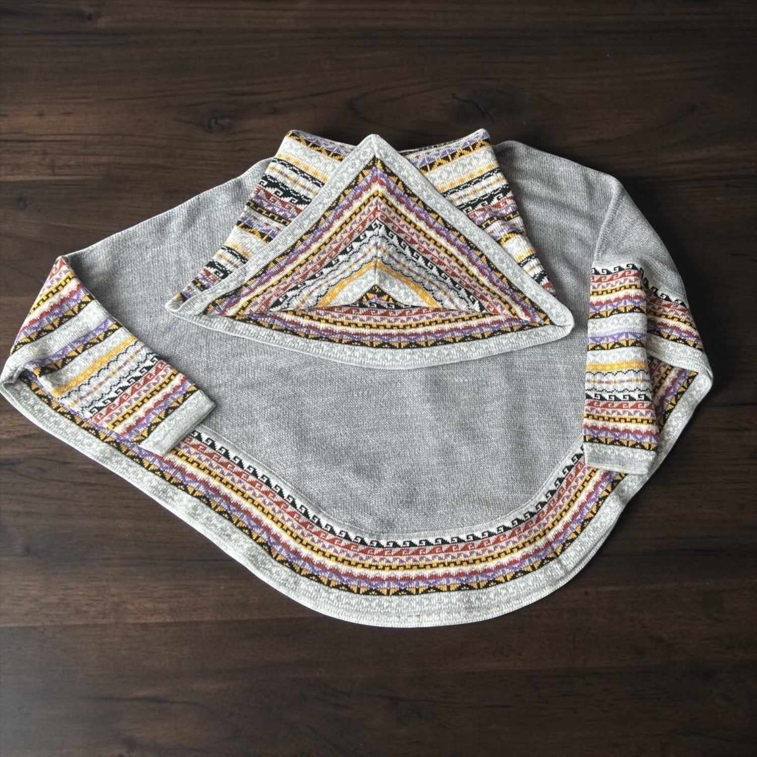 Peruvian Accent grey alpaca poncho with sleeves featuring a colorful geometric pattern on the collar and cuffs.