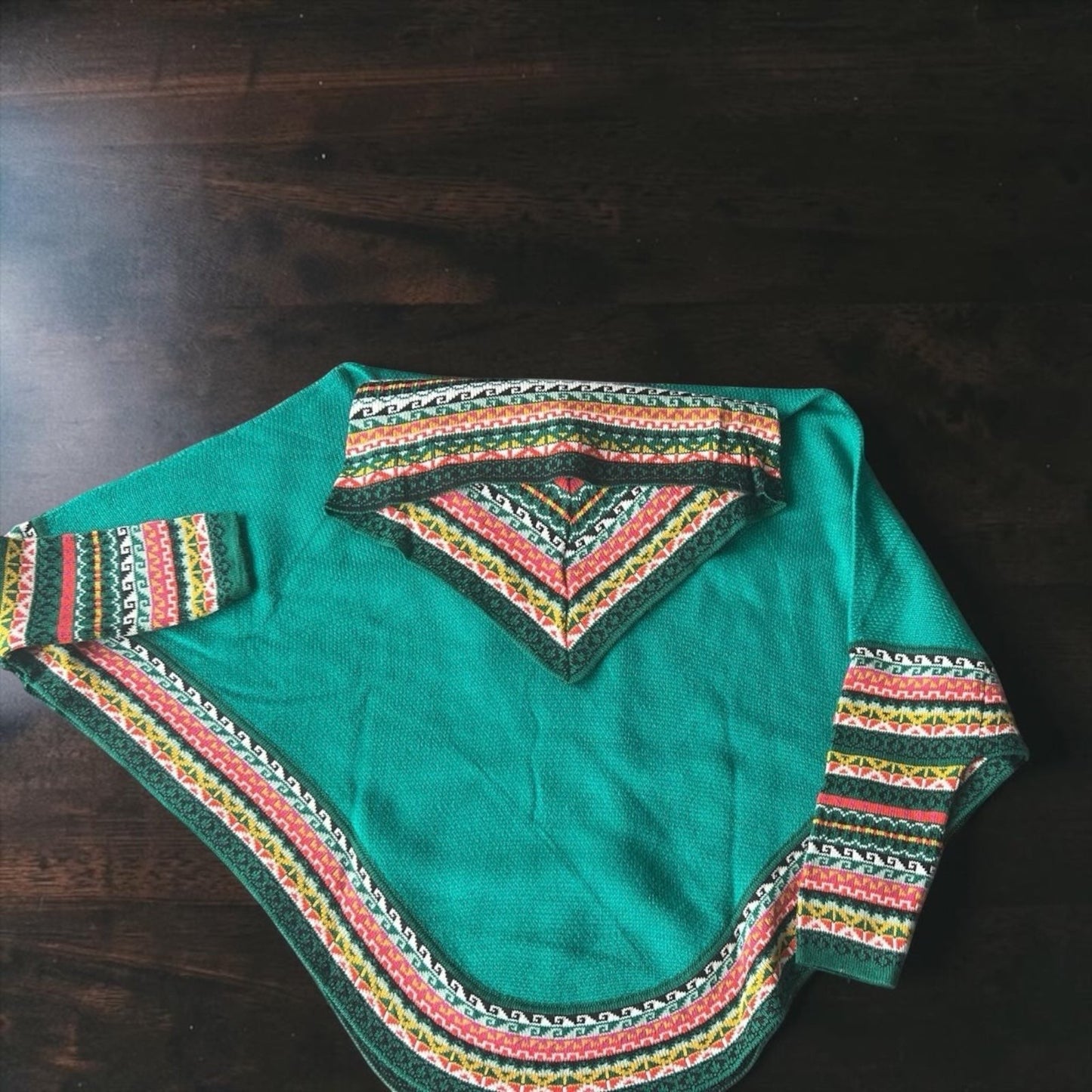Peruvian Accent teal alpaca poncho with sleeves and cowl neck, featuring a colorful geometric Andean pattern trim.