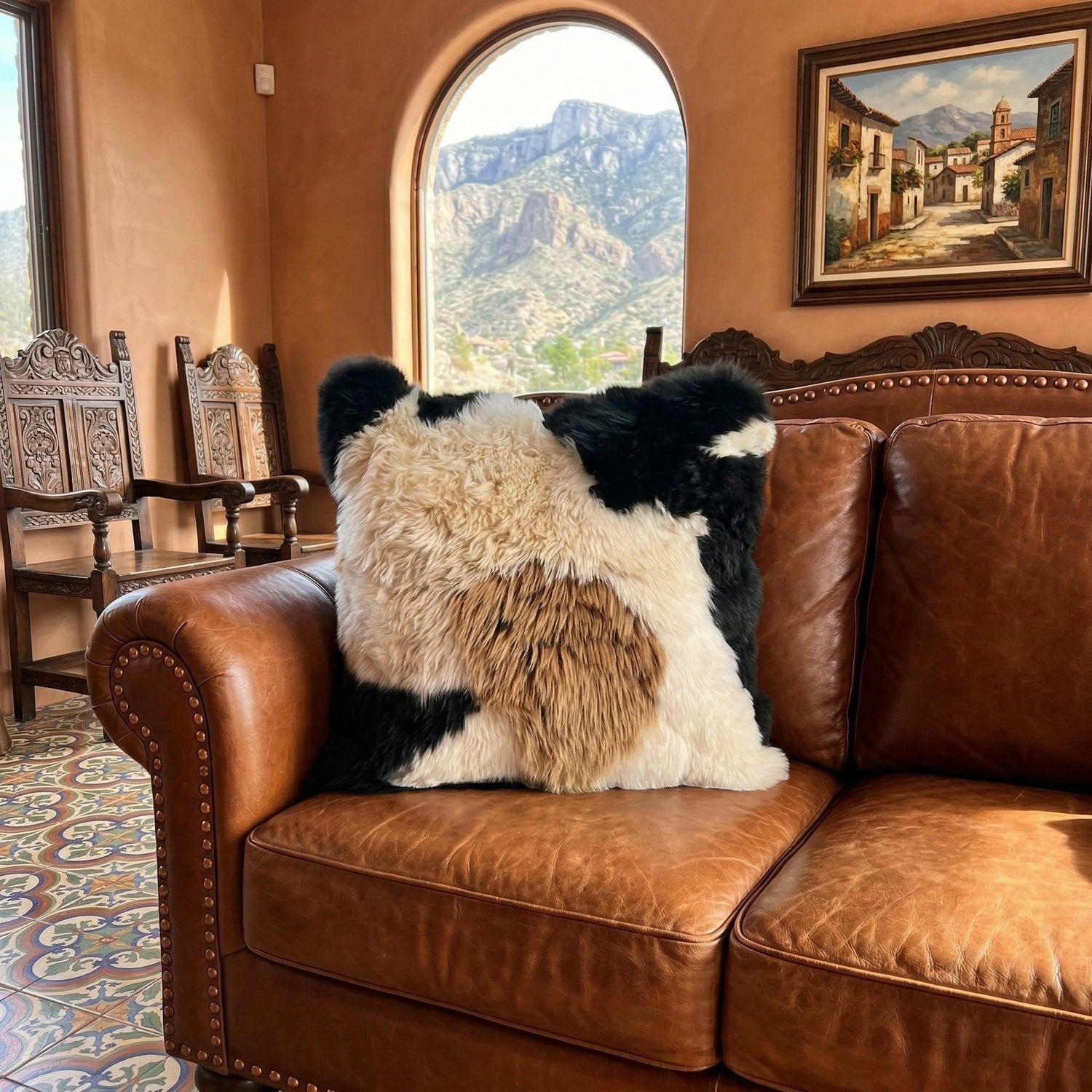 Peruvian Accent mosaic baby alpaca fur pillow with black, cream, and brown patches on a leather couch.