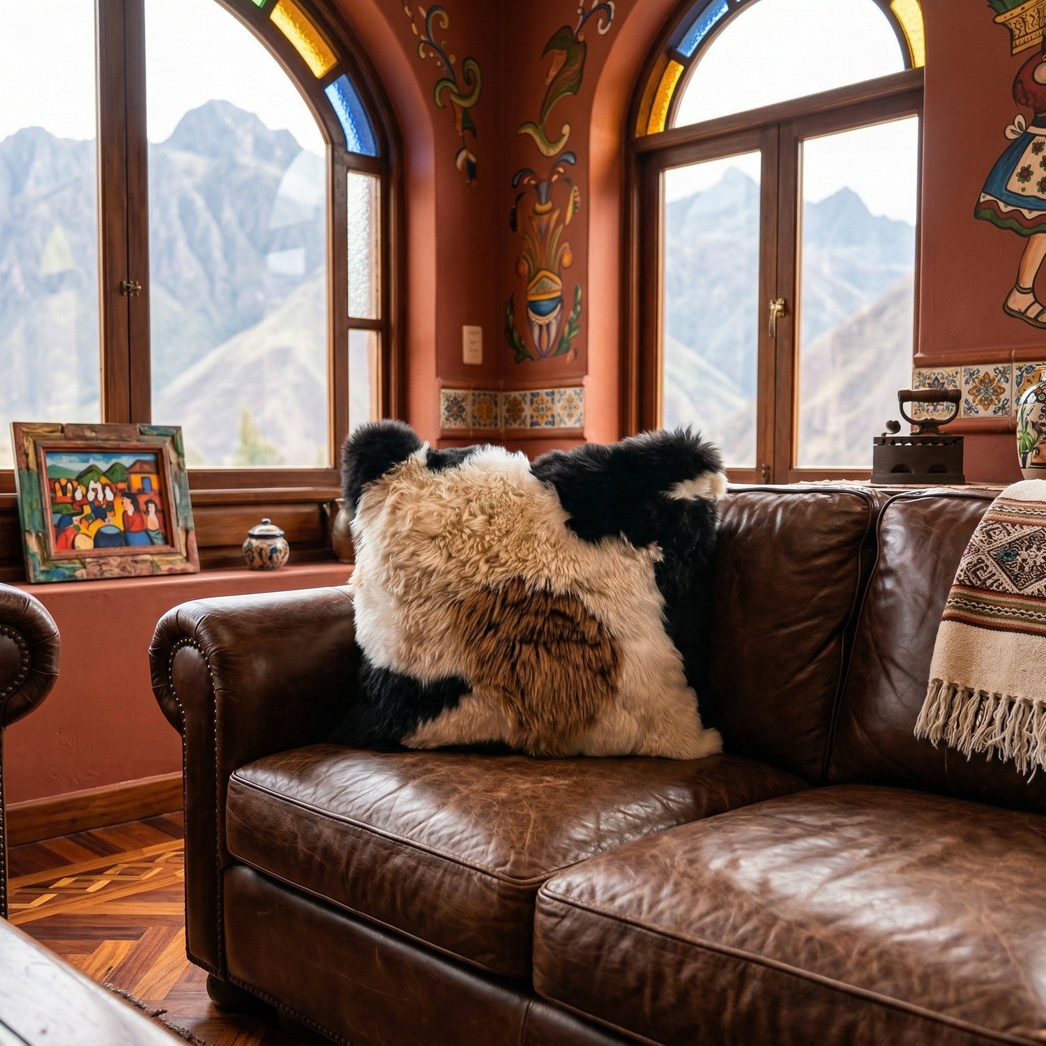 Peruvian Accent mosaic baby alpaca fur pillow with black, white, and brown patches on a leather sofa.