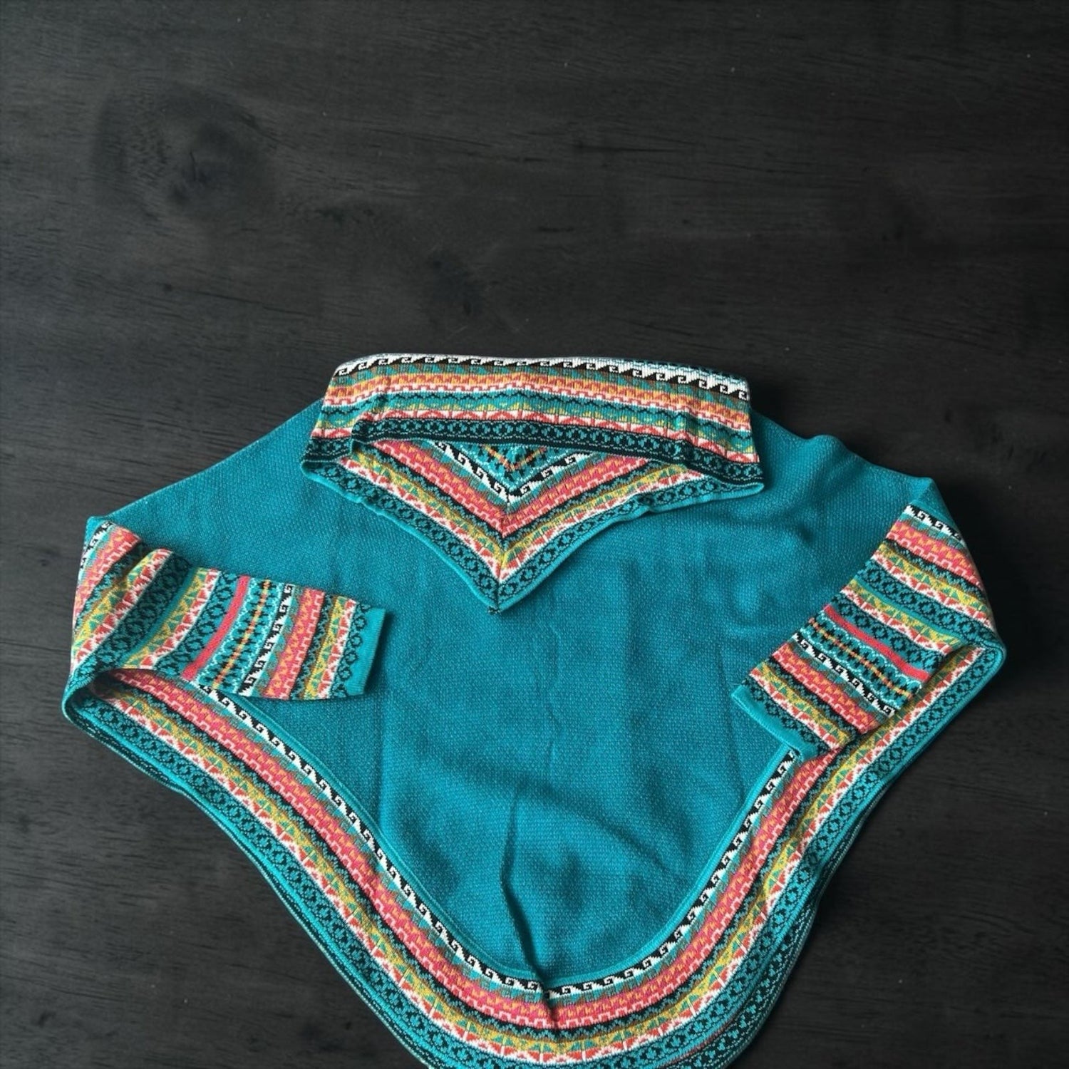 Peruvian Accent teal alpaca poncho with sleeves and a colorful geometric pattern on the collar and cuffs.